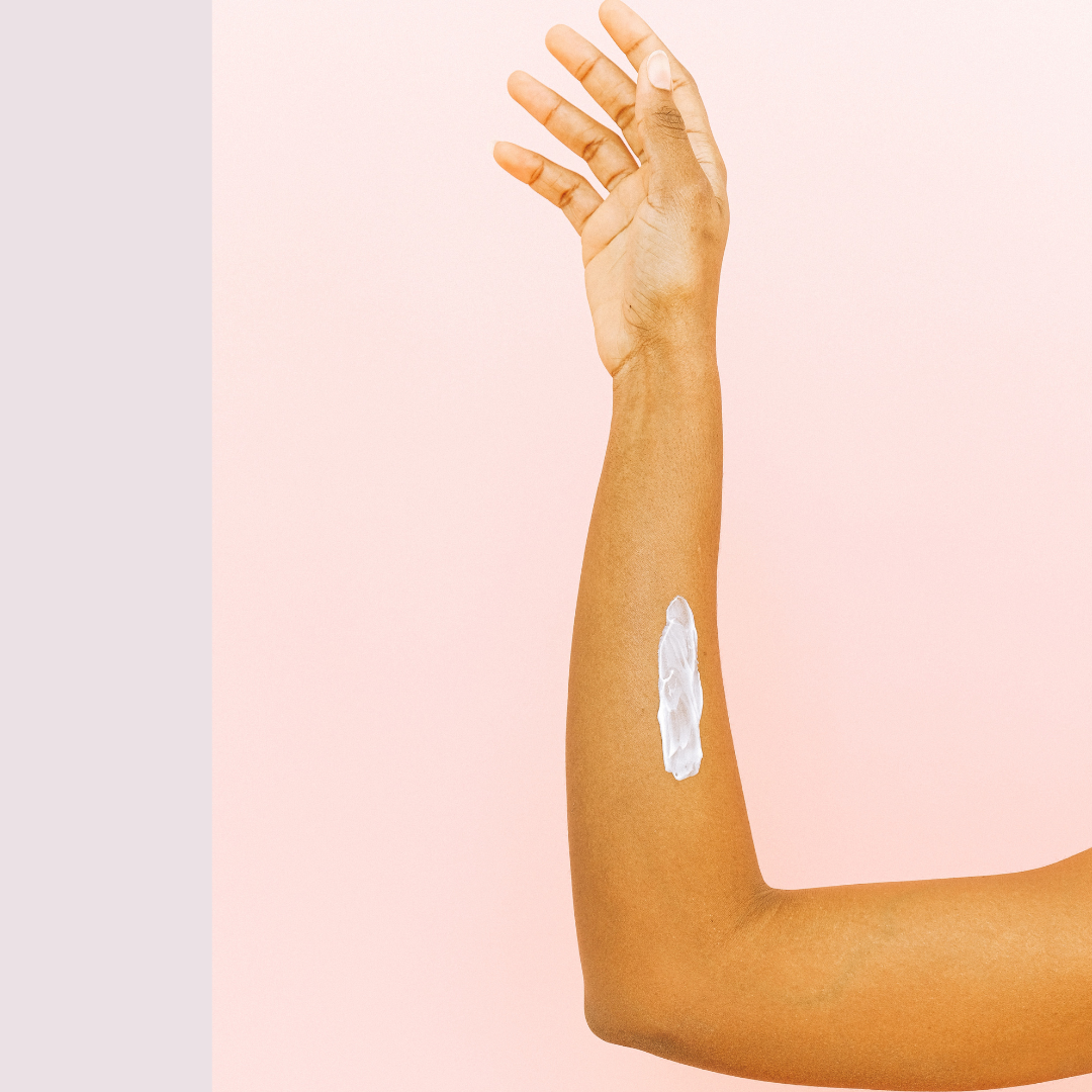 upright tan arm against pink background with self-tanner lotion