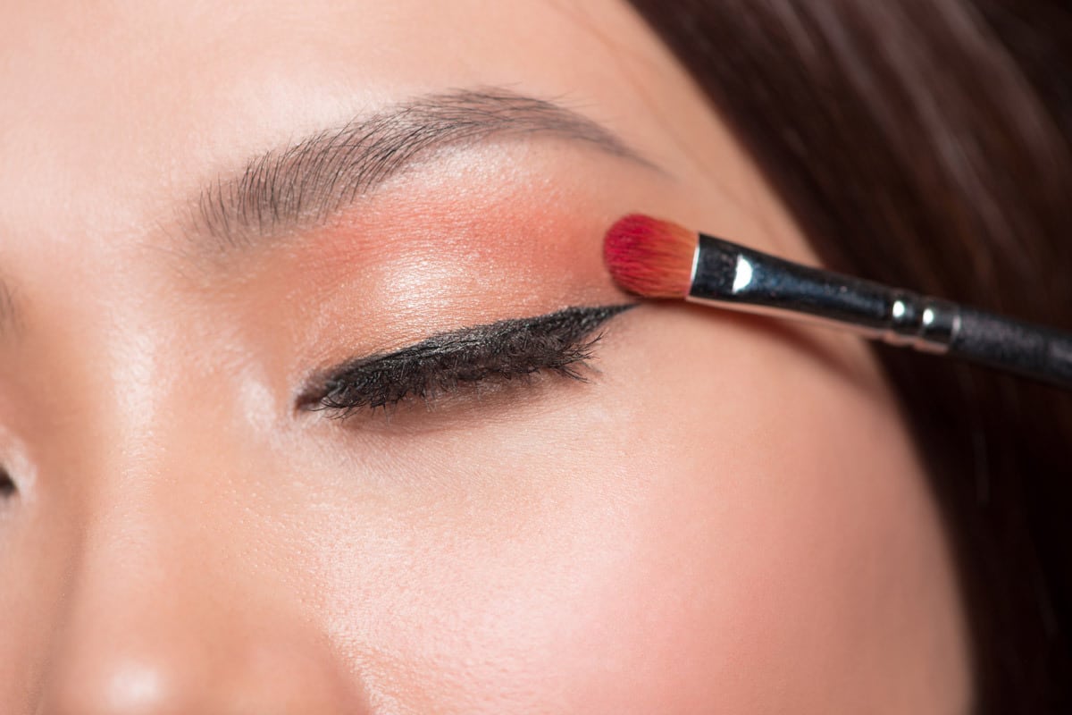 close-up of a woman's closed eye with winged eyeliner as she applies colorful eyeshadow