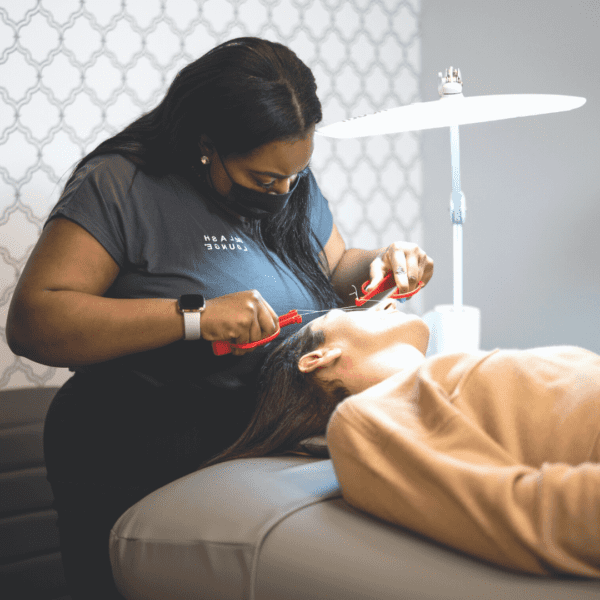 the lash lounge lash stylist performing a brow service on a female guest