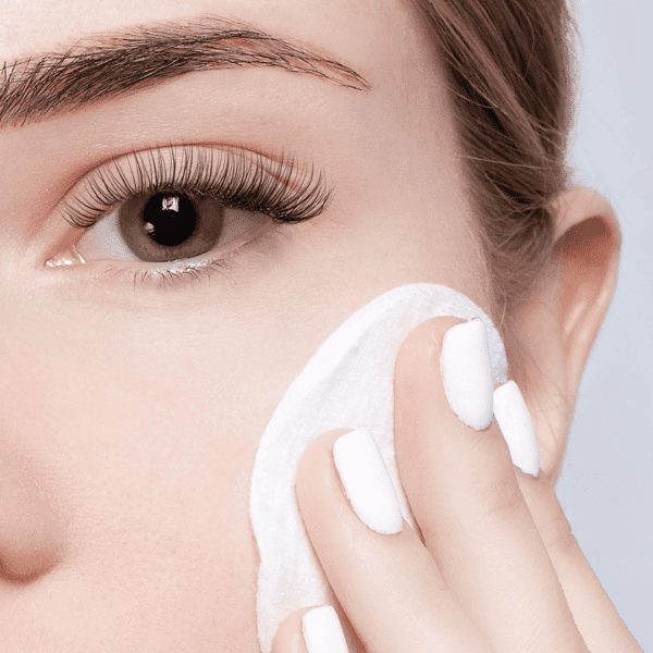 closeup of woman with lashes with a makeup remover pad to her face