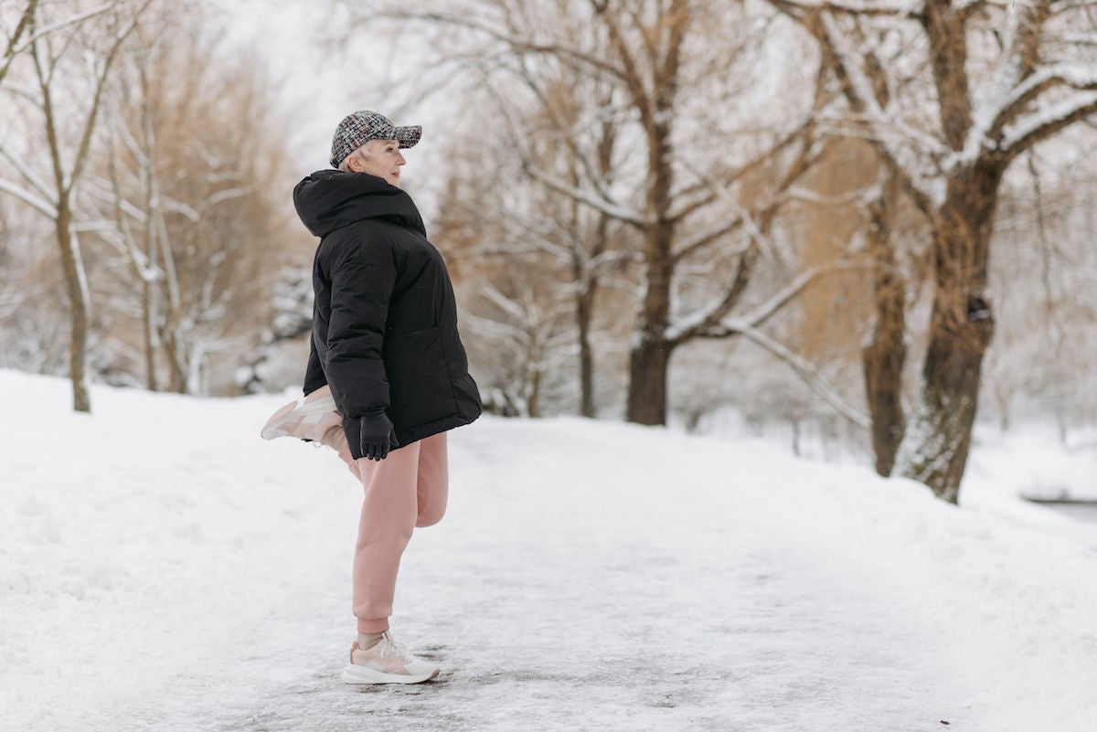 middle aged woman standing in snow stretching