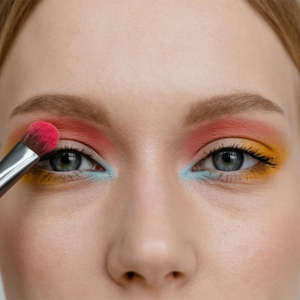 close-up of a woman&#039;s face as she applies colorful summer eyeshadow