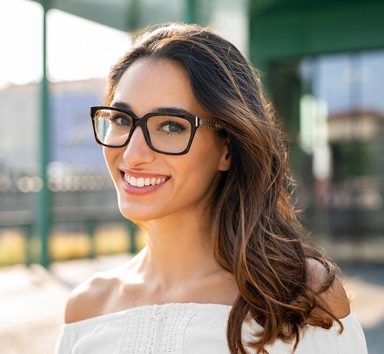 young brunette woman smiling while wearing stylish glasses and lash extensions
