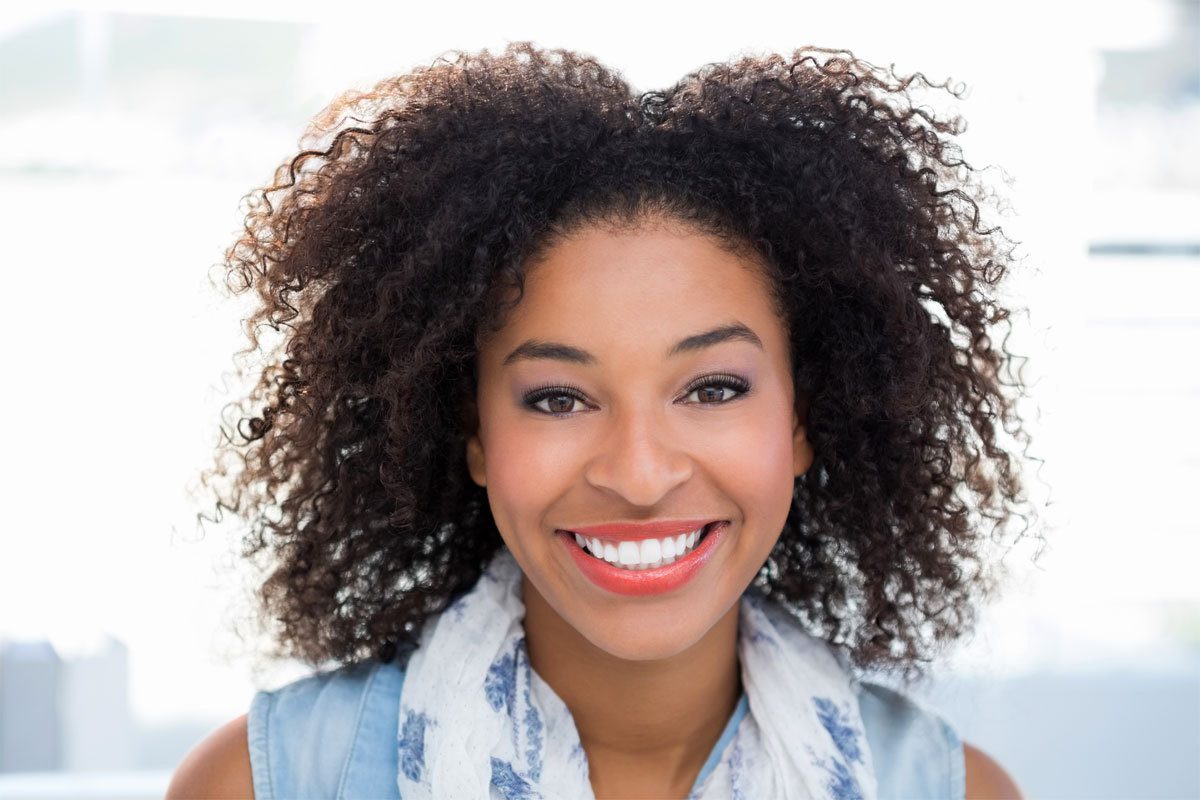 A woman, with a fresh face of makeup and a natural lash extension look, looks at the camera and smiles