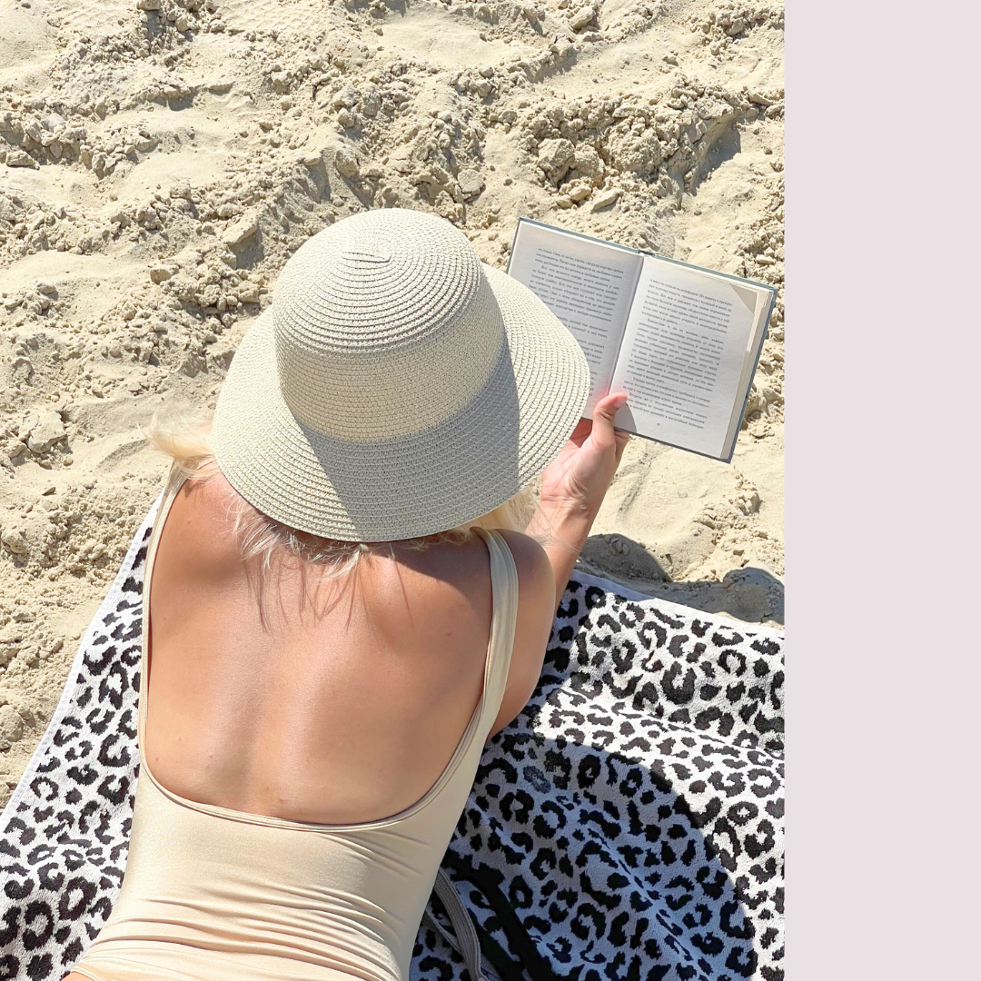 woman laying on stomach on beach towel with hat