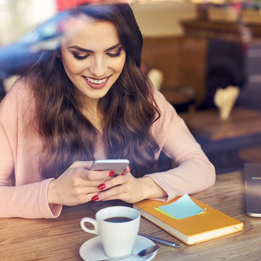 woman holding her phone and smiling while drinking coffee
