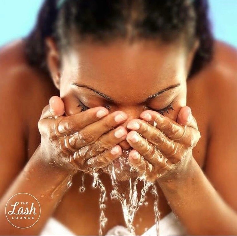 Black woman standing at sink washing her face to achieve clean lashes