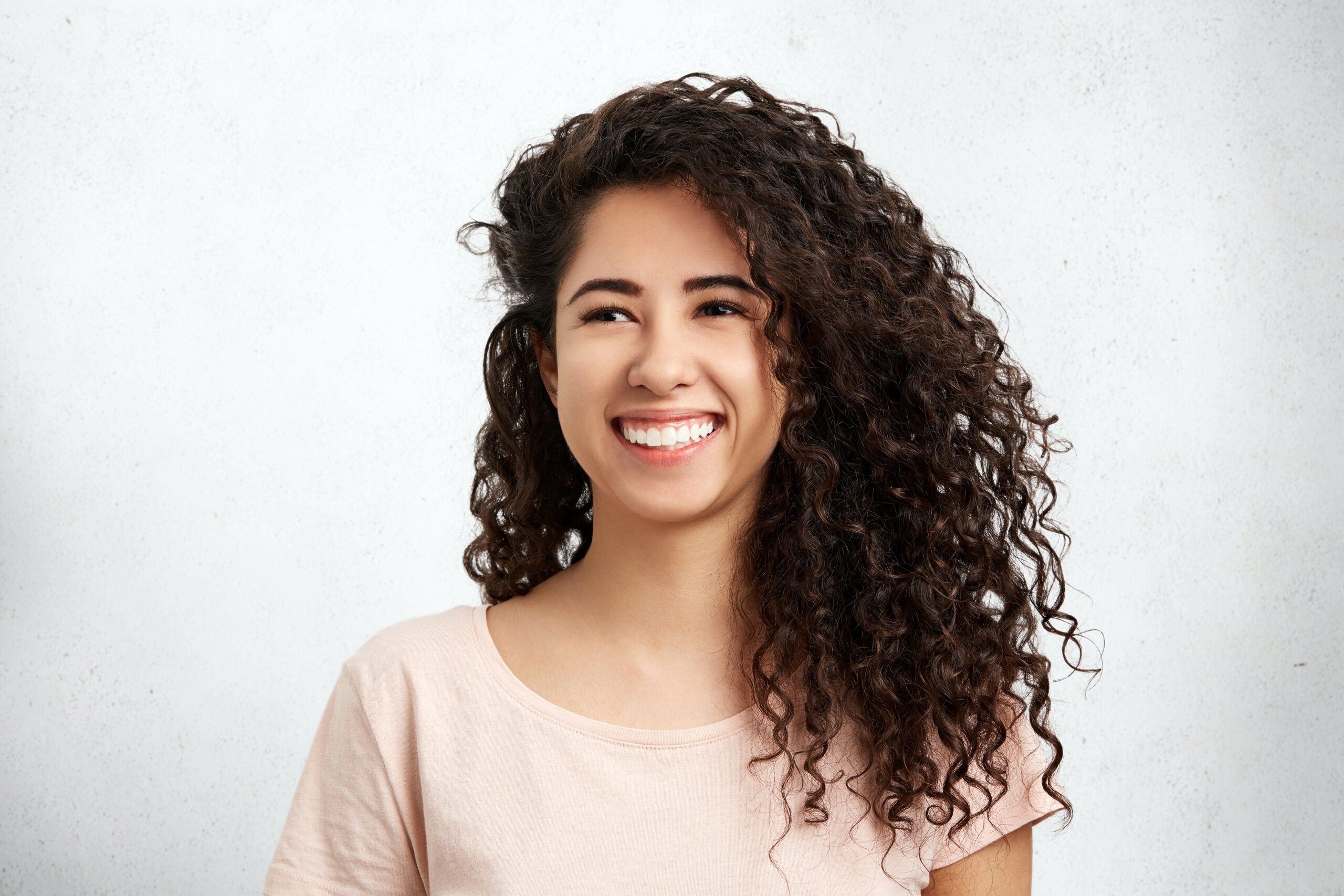 Young woman with curly hair smiling with bold brows and wispy lashes