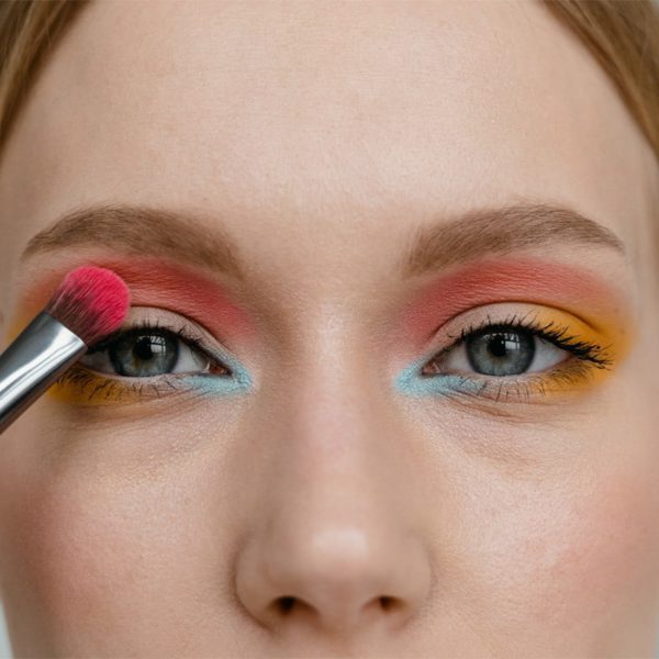 close-up of a woman's face as she applies colorful summer eyeshadow