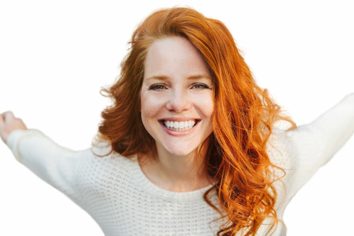 woman with red hair and brow tint smiling with her arms outstretched