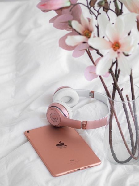 pink headphones and iPad laying on bed with flowers in vase on the right