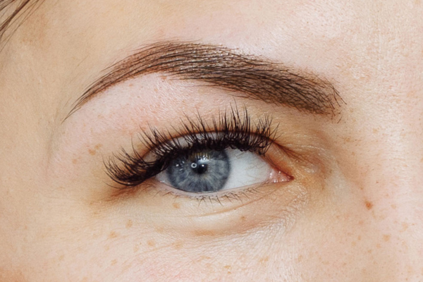 An extreme closeup of a Caucasian woman’s blue eye and eyebrow after receiving permanent makeup services for her eyebrows.
