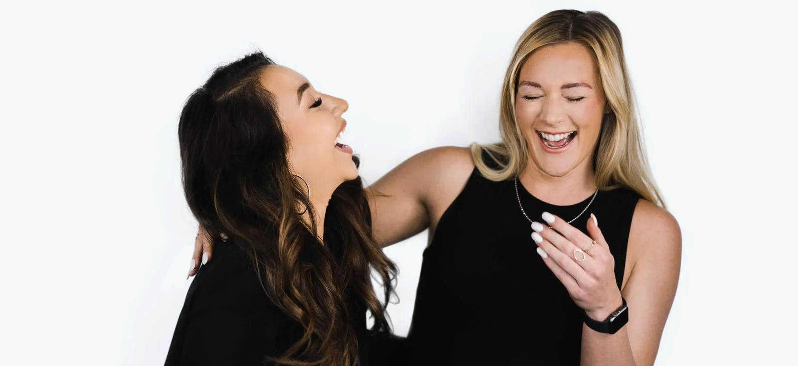 Woman with an eyebrow perm and blonde hair laughs with another woman.