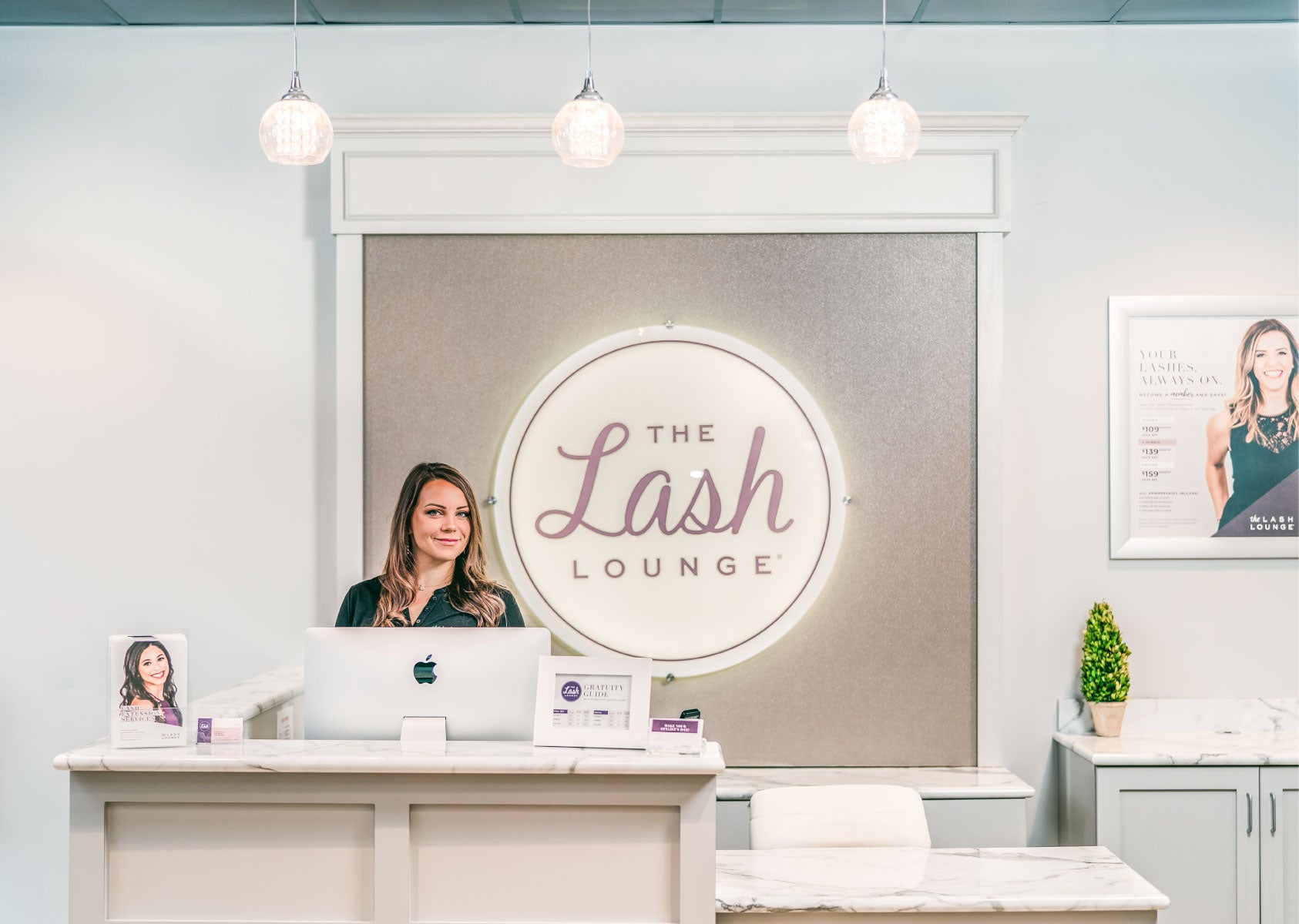 Lash Lounge employee smiling and standing at the front desk inside of the salon.