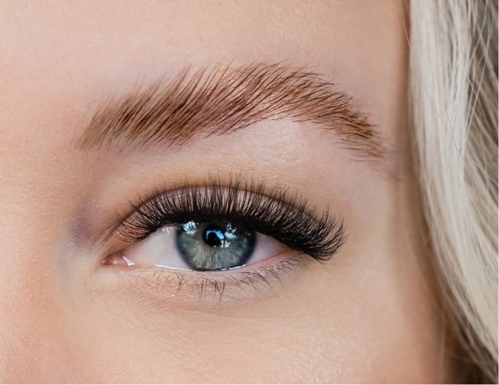 An extreme closeup of a Caucasian woman’s blue eye and eyebrow after receiving a brow lamination service from The Lash Lounge.