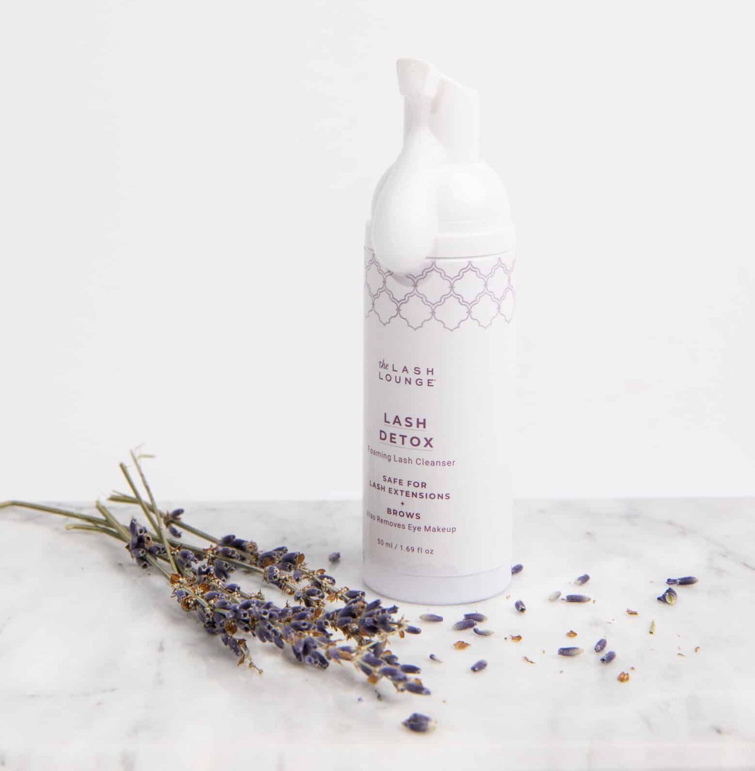Lash Detox foaming cleanser product sitting on a marble countertop with dried lavender surrounding the product.