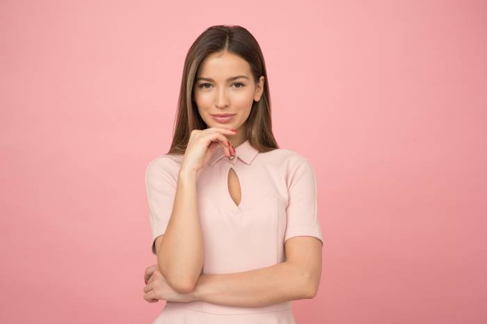 brunette girl in a pink dress poses in front on a pink background