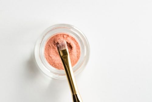 peach colored eyeshadow in a glass pot with a makeup brush