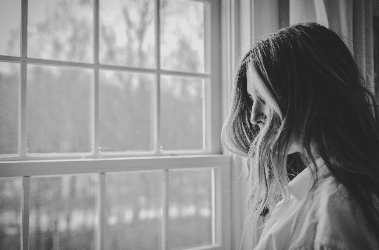 woman with curly hair looking out the window in black and white
