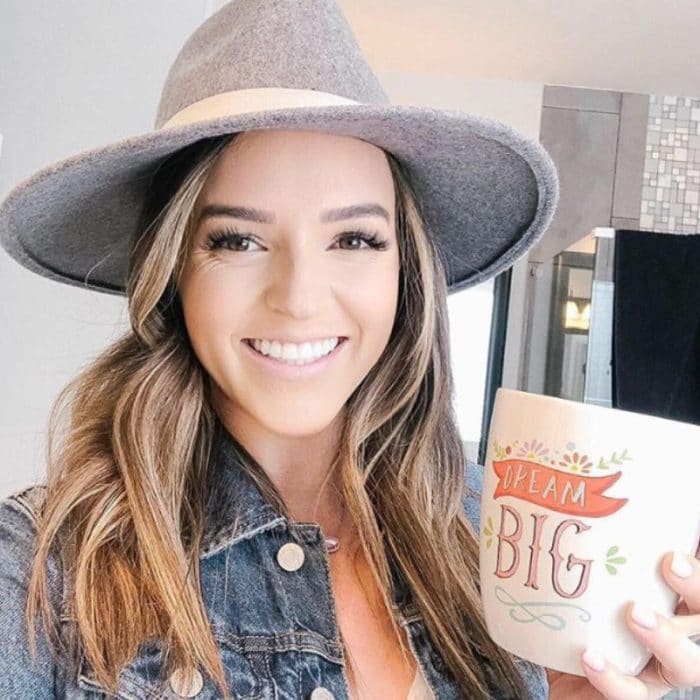 brunette woman with a grey hat holding a mug that says 'Dream Big'
