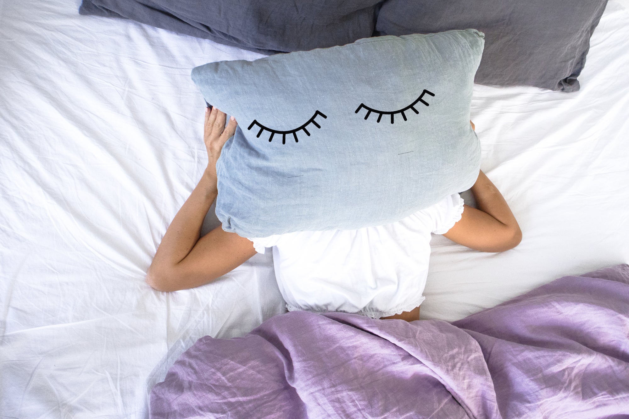 woman in bed with lash design pillow covering her face