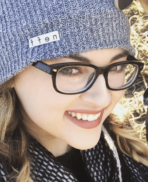 Lash Lounge stylist, Chelbi, wearing a hat and a scarf while smiling for a selfie.