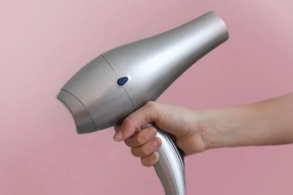 close up of a hand holding a blowdryer in front of a pink wall