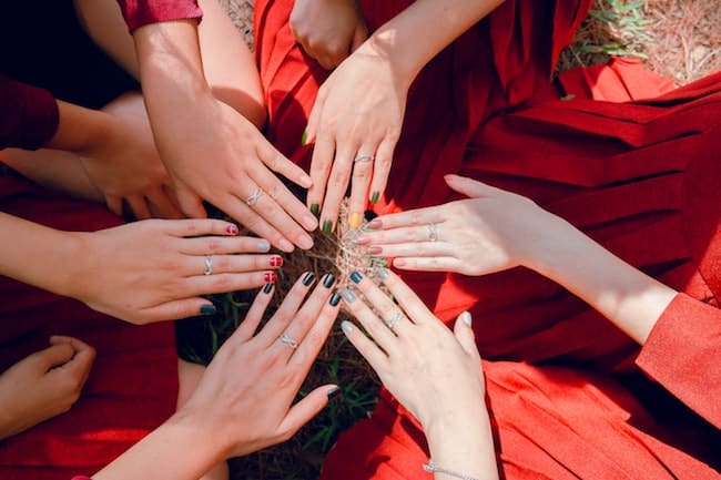 a closeup of 6 hands placed in a circle shape that are painted with nail polish.