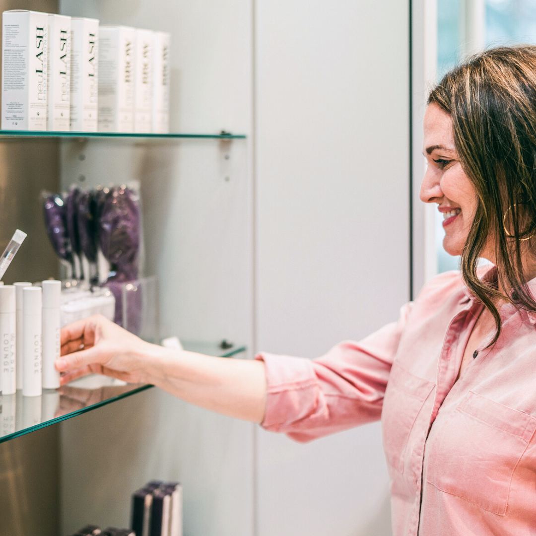 brunette woman standing at Lash Lounge retail wall selecting a product