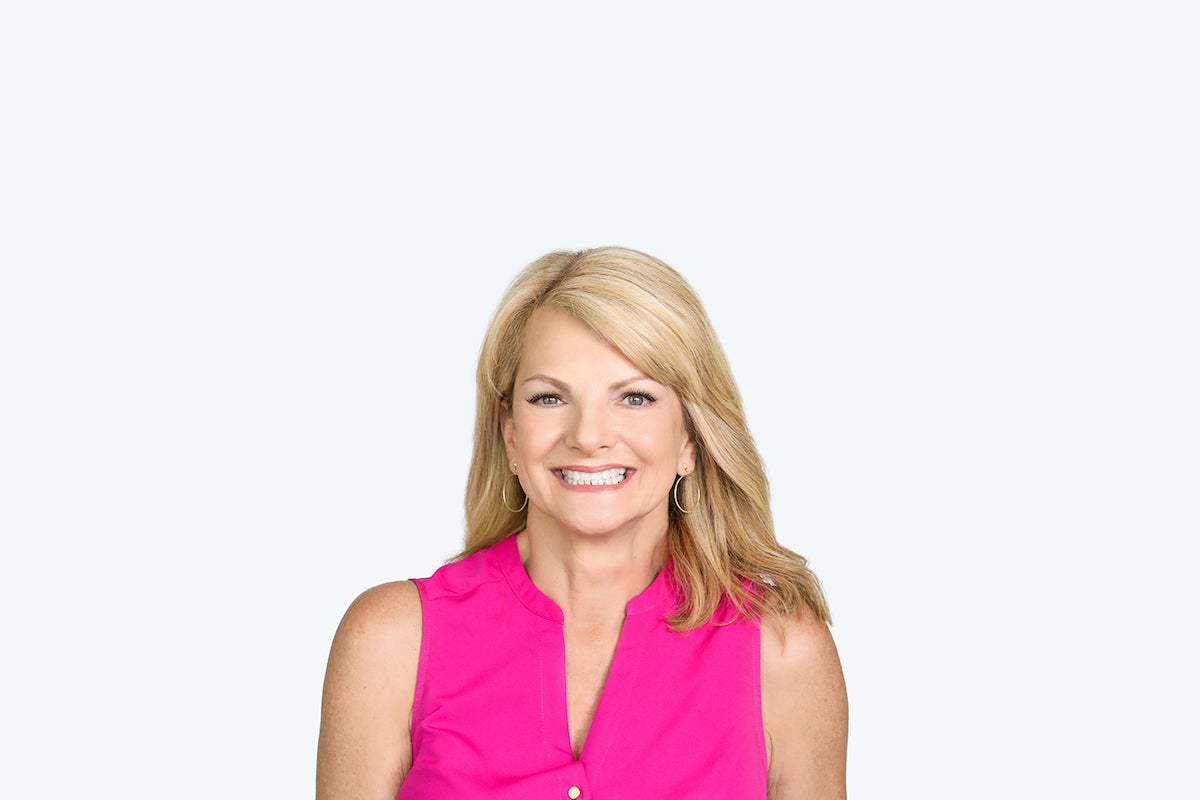 smiling blonde real Lash Lounge woman with classic lash extensions wearing pink in front of white wall