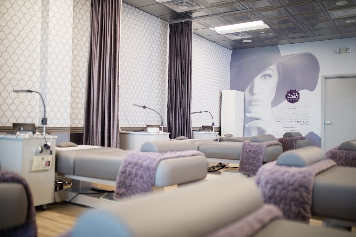The Lash Lounge studio with printed walls, grey beds, purple accents, and stylist stations