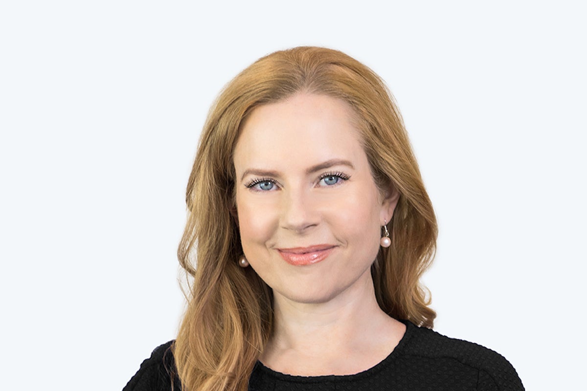 red haired woman smiling wearing a black shirt in front of a wall