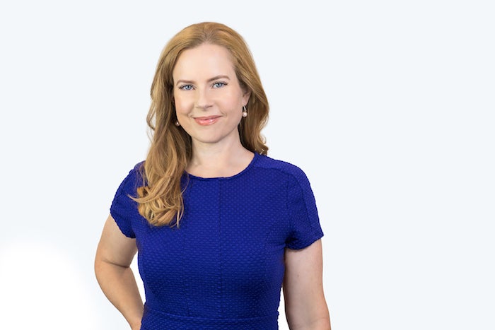 red haired woman smiles standing in front of a plain wall