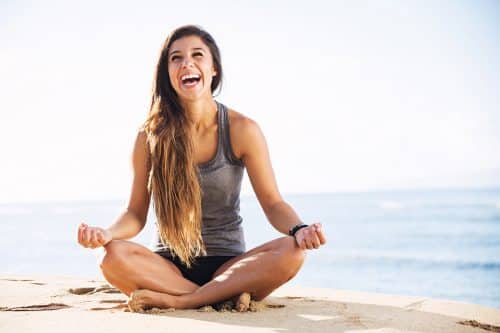 young girl laughing and smiling while doing yoga on a beach