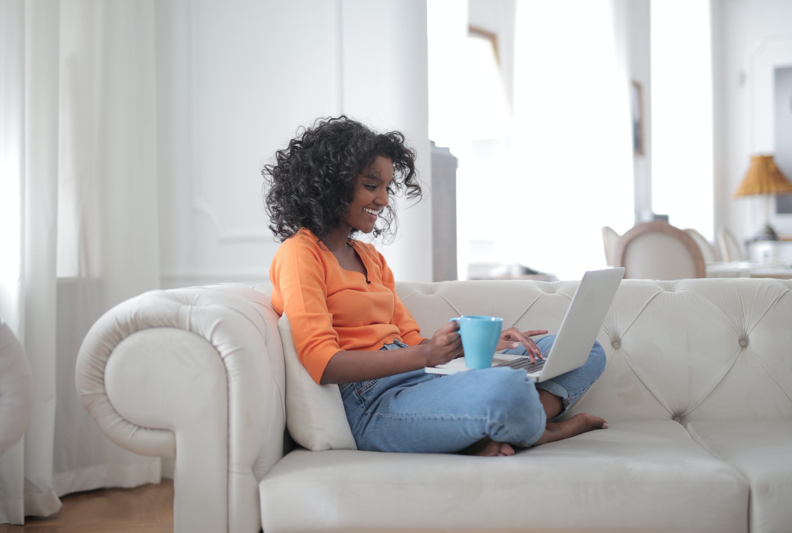 a woman sitting on a couch with coffee and a laptop