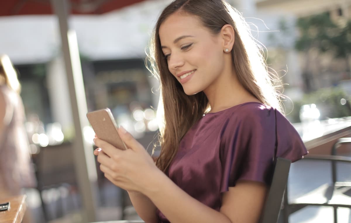 Woman smiling at her social media lash inspo photo on her Iphone wearing a purple shirt