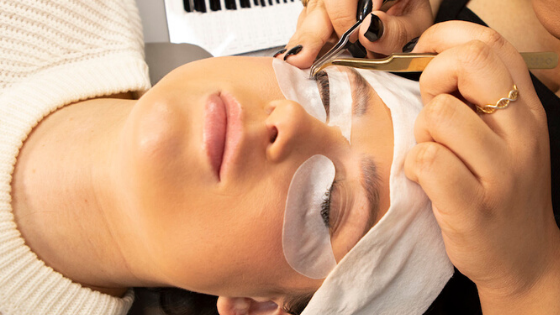 woman lying down with eyes closed while she is getting her eyelash extensions refilled