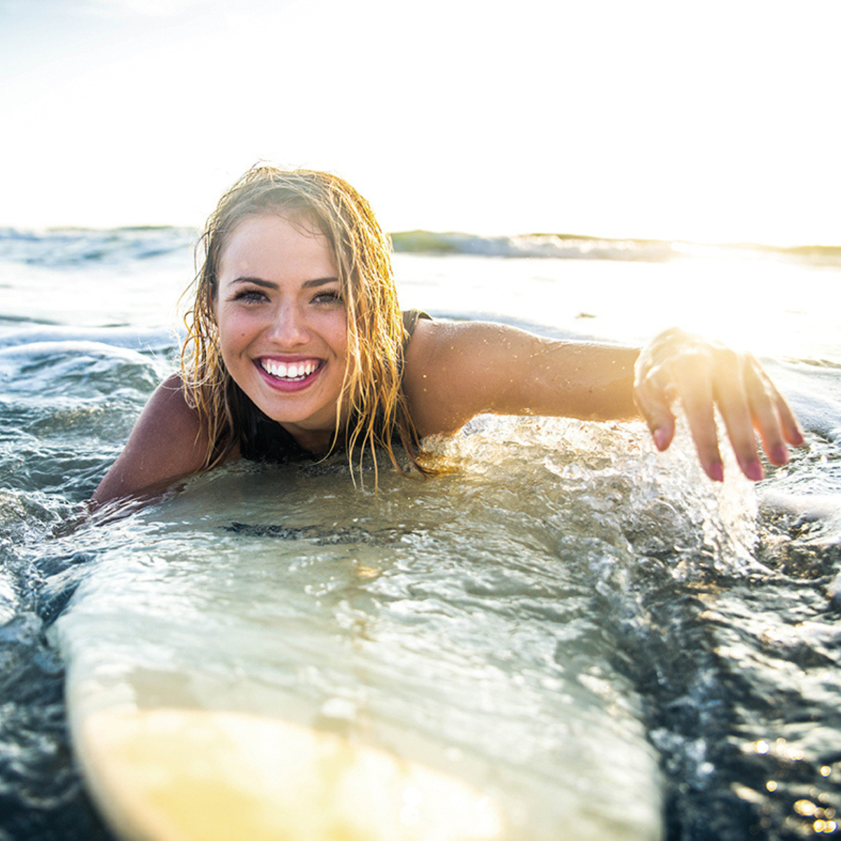 Woman in ocean surfing and swimming with eyelash extensions