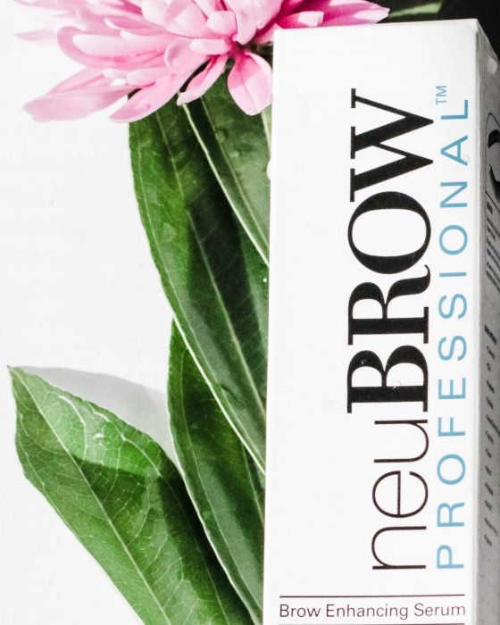 box of brow serum product neuBROW PROFESSIONAL™ with a bright pink flower in the background