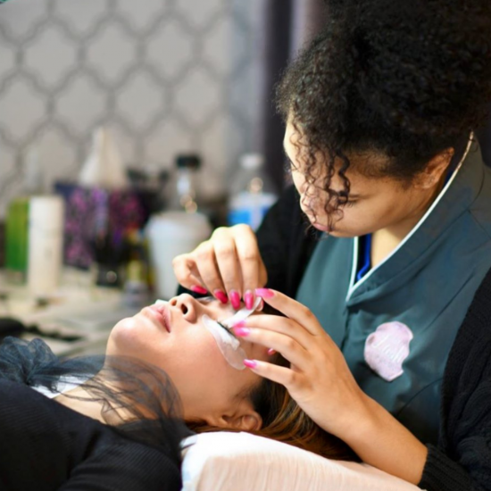 lash extension technician leaning over her female guest while working on her lashes