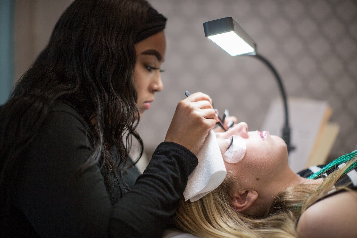 An eyelash technician applying lash extensions on a female guest at The Lash Lounge salon
