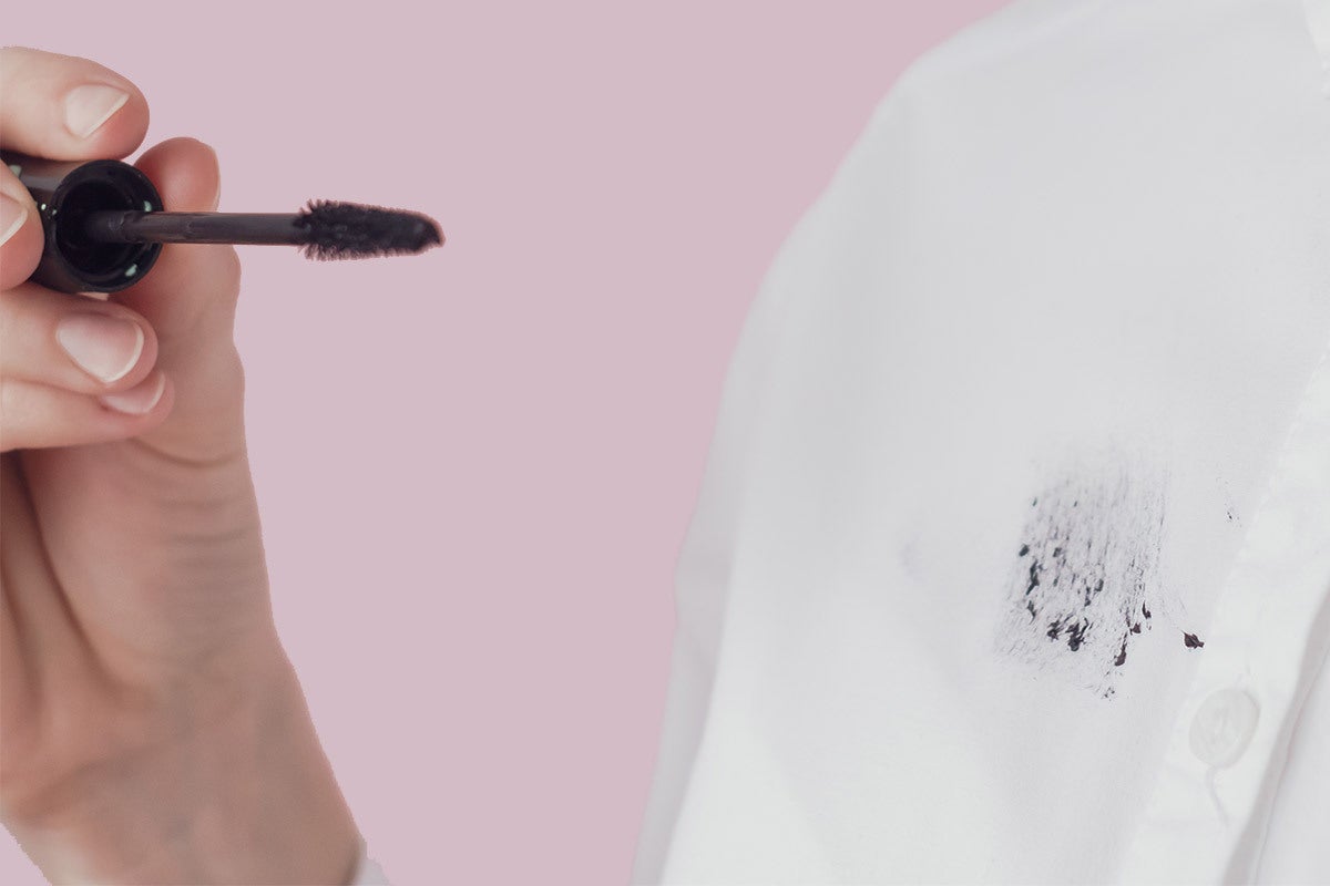 woman's hand holding a mascara wand near her white shirt with mascara stain