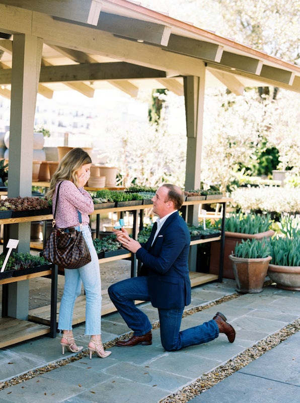 blonde woman with lash extensions standing while man is on one knee proposing