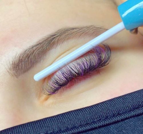 Close-up of a woman's closed eye showing lash extensions with color