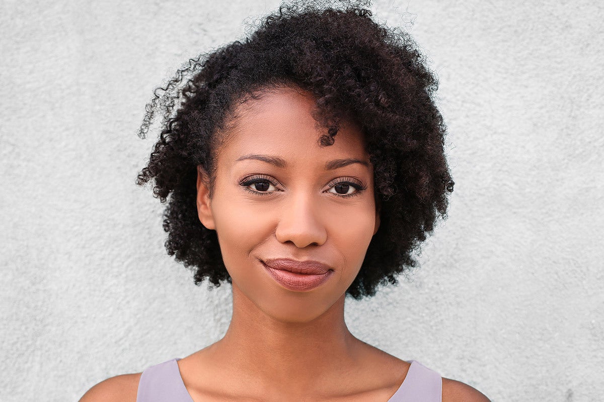 A woman with short, dark, curly hair and lash extensions smiling