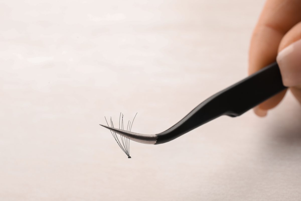 close-up of hand holding tweezers with a cluster of store-bought lashes