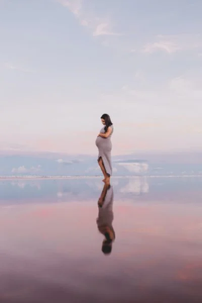 pregnant woman holding her stomach with a beautiful mountain background behind her.