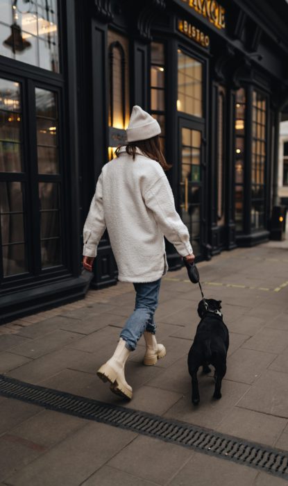 woman wearing coat and hat walking her dog on a city street