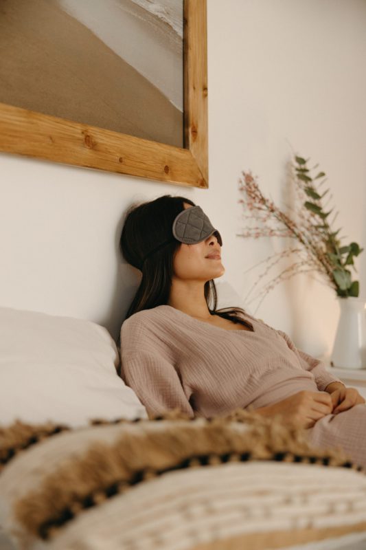 asian woman wearing a sleep mask and relaxing on her bed