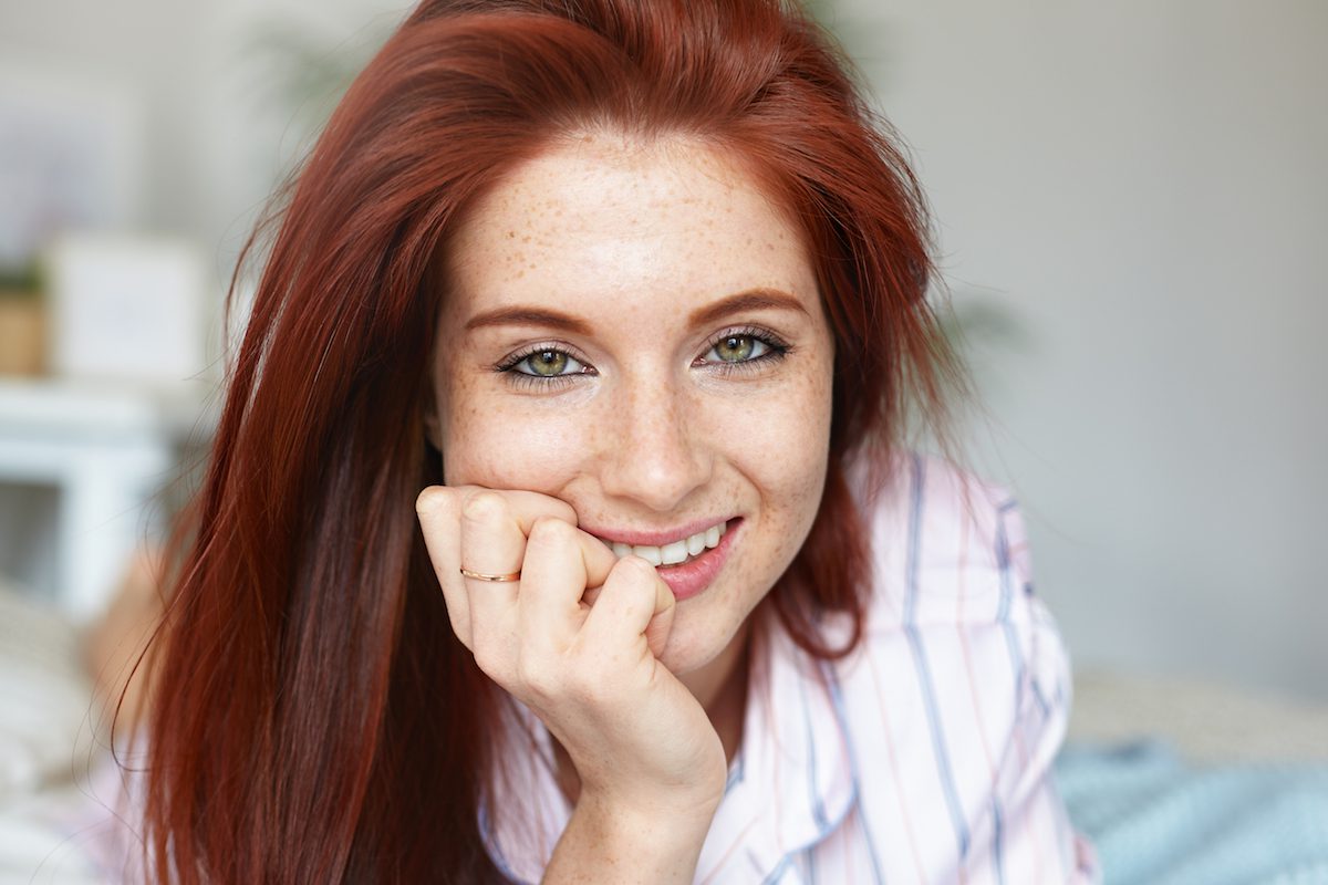 closeup of a young woman with red hair smiling with a brow tint